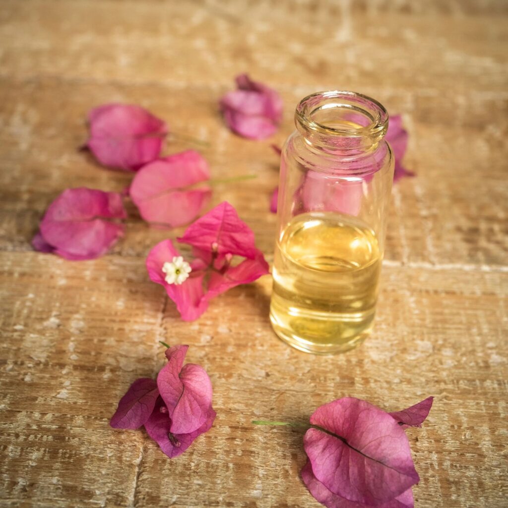 Essential oil in small glass bottle and bougainvillea flowers on wooden background